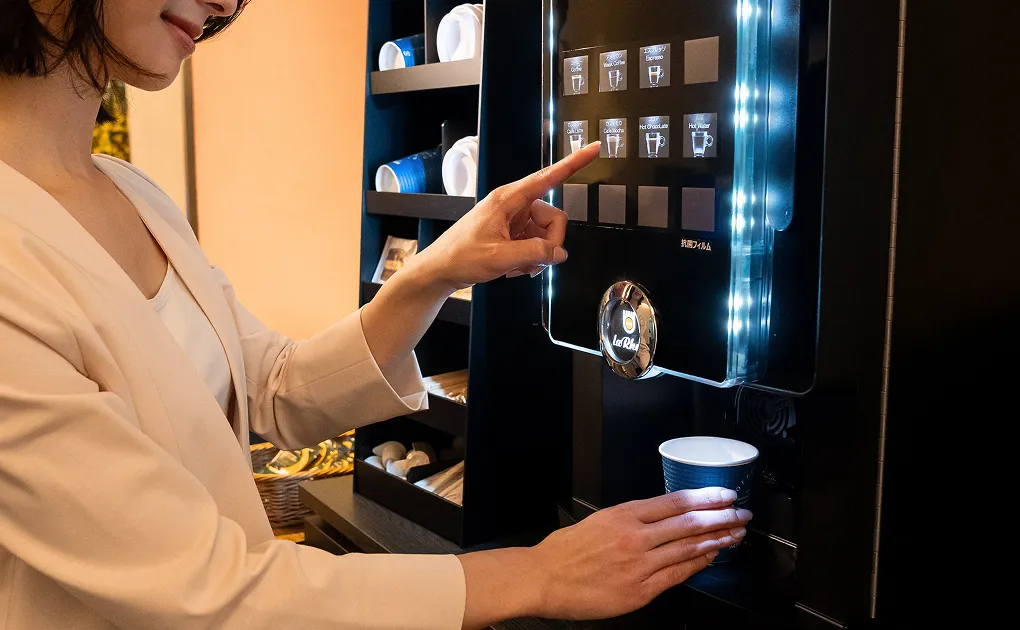 宿泊客が、ロビーにある無料のセルフコーヒーマシンを操作している様子。