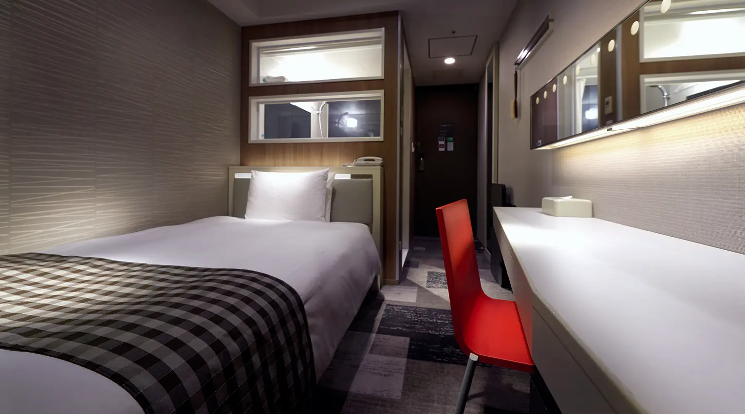 デスクと赤いチェアを備えたコンパクトな客室の室内風景